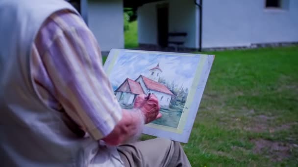 Um artista mais velho está dando seus últimos toques na pintura — Vídeo de Stock