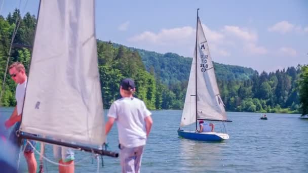 La gente está de pie en una orilla con sus barcos de vela — Vídeo de stock