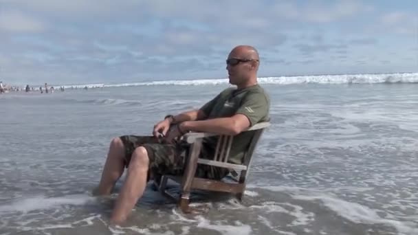 Zittend op een stoel op de oever bespat met golven van de zee — Stockvideo