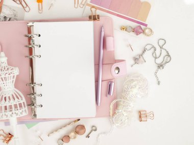 Şirin kırtasiyeli pembe bir planlayıcının üst görüntüsü. Beyaz manken figürlü pembe bir planlamacı. Beyaz arkaplan ve güzel aksesuar kalemleri, düğmeleri, broşürleri olan bir planlayıcı.