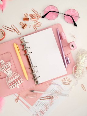 Şirin kırtasiyeli pembe bir planlayıcının üst görüntüsü. Beyaz manken figürlü pembe bir planlamacı. Beyaz arkaplan ve güzel aksesuar kalemleri, düğmeleri, broşürleri olan bir planlayıcı.