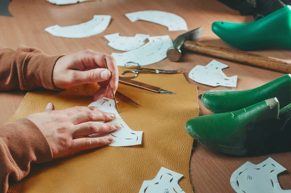 Shoemaker making patterns from yellow leather on the table
