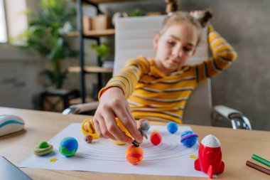 8 yaşında bir kız, gezegenlerle ve oyuncak uzaylılarla oynuyor. Odadaki masada oturuyor. Ödevini yapan kız ilkokul öğrencisi çocuk kilinden ya da plastikten gezegen modelleri yapıyor. Astronota odaklanın..