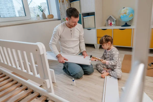 Tochter mit Hammer hilft ihrem Vater die Schublade des Kinderbettes zu reparieren — Stockfoto