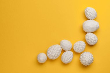Beyaz Paskalya yumurtaları, geometrik desenli sarı arkaplanlı ve mesaj için boş alanı olan. Üst manzara, düz uzanma.