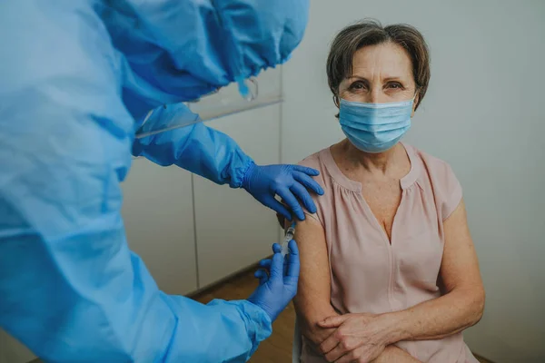 Doctor in protective overall and gloves making COVID-19 vaccination