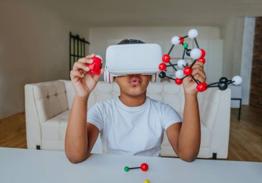 VR gözlük kullanan bir çocuk moleküler model tutuyor ve evde kimya dersi alıyor..