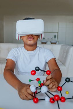 VR gözlük kullanan bir çocuk moleküler model tutuyor ve evde kimya dersi alıyor..