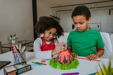 Kız ve erkek kardeş okul projesi için çocuklardan volkan modeli yaparak eğleniyorlar. Ev eğitimi kavramı.