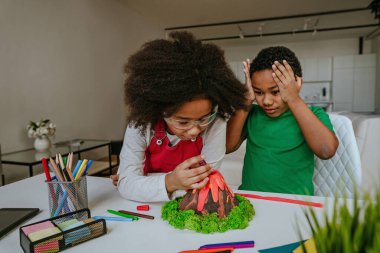 Kız ve erkek kardeş okul projesi için çocuklardan volkan modeli yaparak eğleniyorlar. Ev eğitimi kavramı.
