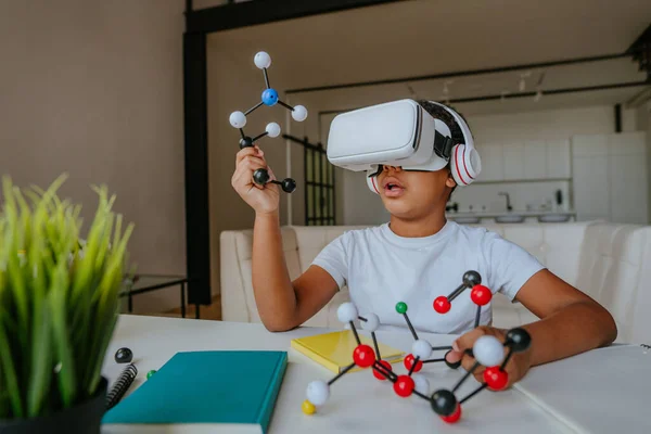 Boy using VR glasses holding molecular model learning chemistry science at home.