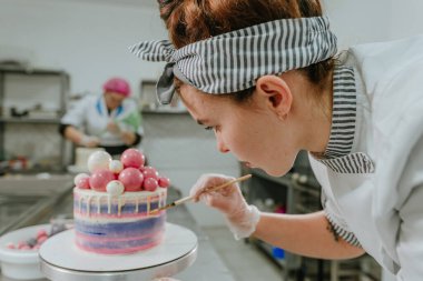 Yenebilir altın boya ve fırça kullanarak doğum günü pastasını dekore eden kadın pastacıya yaklaş.
