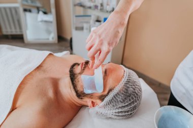 Estetisyen, güzellik salonundaki bir adam için yosun maskesi kullanarak yüz temizleme işlemi yapıyor.