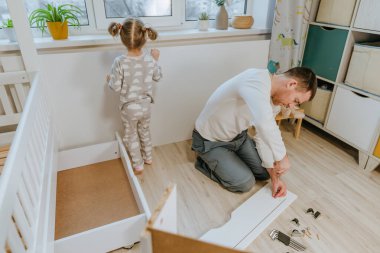 4 yaşındaki küçük bir kız, babasının yatak odasındaki yatağı monte etmesine ya da tamir etmesine yardım eder..