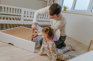 4 yaşındaki küçük bir kız, babasının yatak odasındaki yatağı monte etmesine ya da tamir etmesine yardım eder..