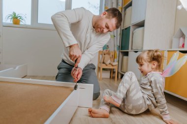 4 yaşındaki küçük bir kız, babasının yatak odasındaki yatağı monte etmesine ya da tamir etmesine yardım eder..