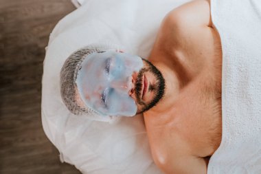 Güzellik salonunda yüzünde yosun maskesi olan bir adam.