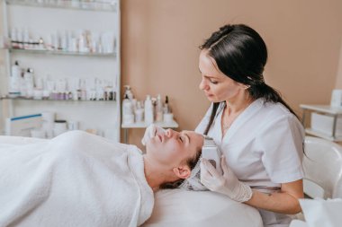 Estetisyen bir güzellik salonunda ultrasonik temizleme spatulası kullanarak yüz temizleme işlemi yapıyor.