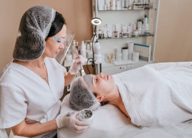Güzellik salonunda bir kadına kilden maske takan estetikçi ya da cilt bakım uzmanı.