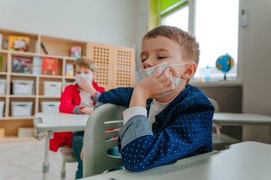 COVID-19 salgını sırasında koruyucu yüz maskesi takan ilkokul öğrencisi. Sosyal mesafe kavramı. Yeni normal eğitim konsepti. Seçici odak.