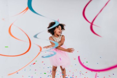 Parti şapkalı mutlu kız beyaz arka planda dans ediyor. Yılanbalığı ve konfetiyle süslenmiş.