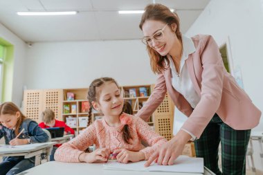 Female teacher helping schoolgirl pointing on something at her notebook