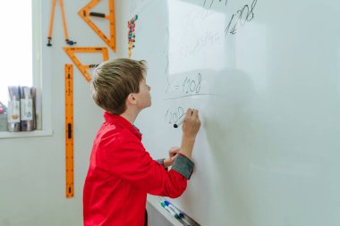 Elementary school student writing on the blackboard by felt-tip in the classroom