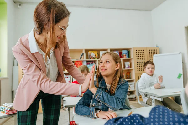 Female teacher helping schoolgirl pointing on something at her notebook