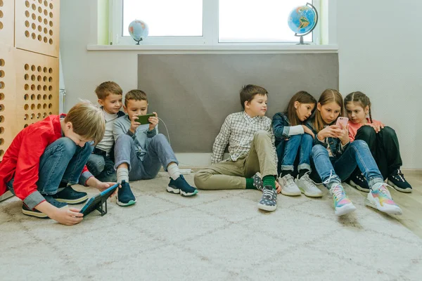 Grupul de adolescenți care stau în sala de clasă de pe podea folosind smartphone-uri — Fotografie, imagine de stoc