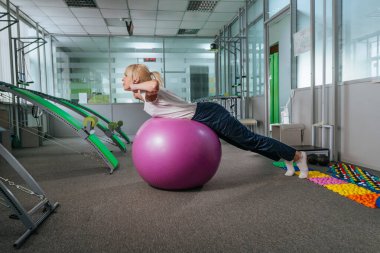 Rehabilitasyon merkezinde topla egzersiz yapan genç bir kadın.