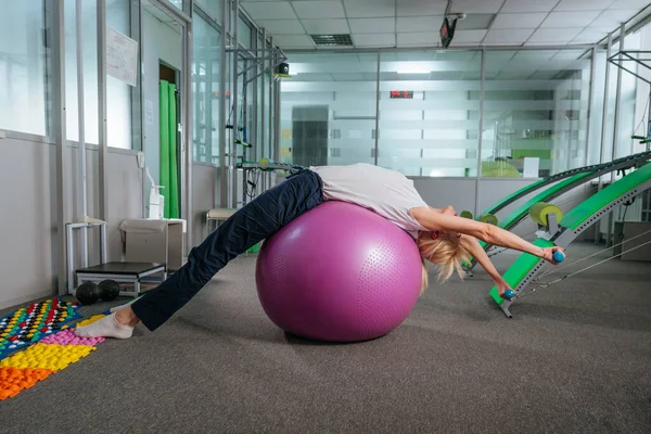 Молодая женщина делает упражнения с мячом для восстановления в реабилитационном центре тренажерный зал — стоковое фото