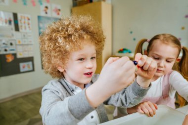 Anaokulunda ya da kreşte oyun öğrenme. Anaokulu öğrencileri, içinde kinetik kum olan bir kabın içinde ahşap boncuklar arıyor ve onları renklerine göre sıralıyorlar. Eğitim konsepti. Seçici odak.