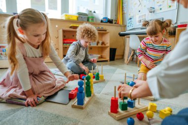 Anaokulu öğrencileri, tahta geometrik oyuncak toplarını ve yerde oturan küpleri sıralıyorlar. Anaokulunda ya da kreşte oyuncak öğrenmek. Eğitim konsepti. Seçici odak.