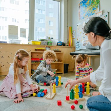 Anaokulu öğrencileri, tahta geometrik oyuncak toplarını ve yerde oturan küpleri sıralıyorlar. Anaokulunda ya da kreşte oyuncak öğrenmek. Eğitim konsepti. Seçici odak.