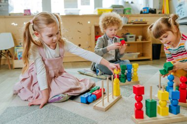 Anaokulu öğrencileri, tahta geometrik oyuncak toplarını ve yerde oturan küpleri sıralıyorlar. Anaokulunda ya da kreşte oyuncak öğrenmek. Eğitim konsepti. Seçici odak.