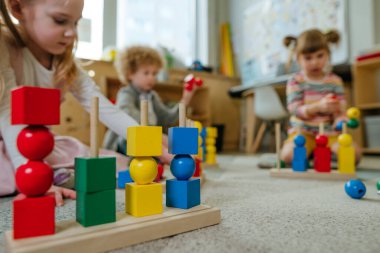 Anaokulu öğrencileri, tahta geometrik oyuncak toplarını ve yerde oturan küpleri sıralıyorlar. Anaokulunda ya da kreşte oyuncak öğrenmek. Eğitim konsepti. Seçici odak.
