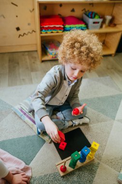 Anaokulu öğrencisi, tahta geometrik oyuncak topları ve yerde oturan küpleri ayırıyor. Anaokulunda ya da kreşte oyuncak öğrenmek. Eğitim konsepti. Seçici odak.