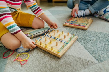 Coğrafi paket lastiğiyle oynayan çocukları kapatın. Uçak geometri şekillerini keşfetmek için kullanılan tahta tahtadan yapılmış matematiksel bir manipülatif. Anaokulunda oyuncak öğrenmek. Eğitim konsepti. Seçici odak.