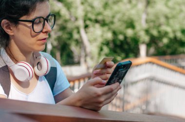 Kulaklıklı genç bir kadın kredi kartıyla ödeme yapıyor.