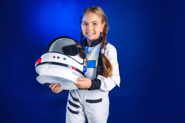 Astronot kostümü ve kask giyen genç kız telif alanı olan koyu mavi arka planda duruyor. Uzay elbisesi içindeki güzel kızın portresi..