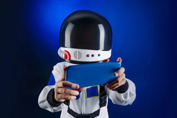 青少年穿着航天服 头戴安全帽 用智能手机发短信或带着自己站在带有复制空间的深蓝色背景上 — 图库照片