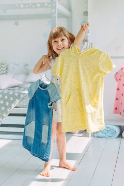 Güzel küçük kız çocuk odasında bir elbise seçiyor. Seçici odak.