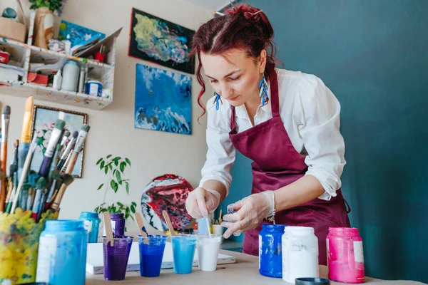 Female artist pouring acrylic medium for painting picture in fluid