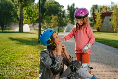 Küçük tatlı kız büyükannesine kask takarak paten kaymaya hazırlanırken yardım ediyor.