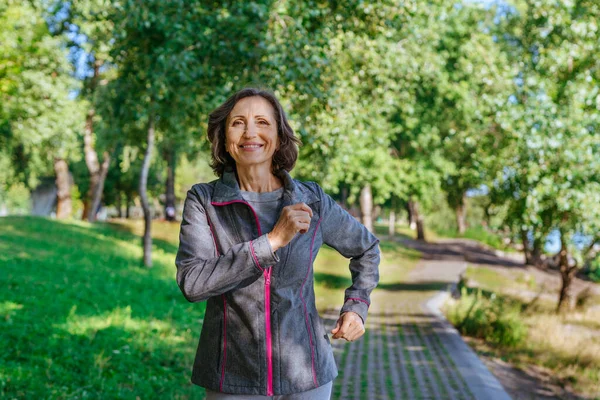 Parkta spor kıyafetleri içinde koşan mutlu olgun bir kadın..