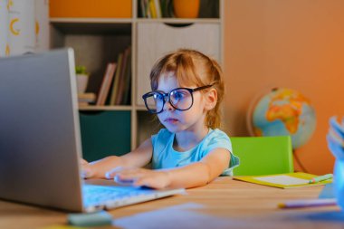 İlkokul öğrencisi evde bilgisayarla ders çalışıyor. Odadaki masada oturuyor. Salgın tecrit konsepti sırasında uzaktan eğitim.