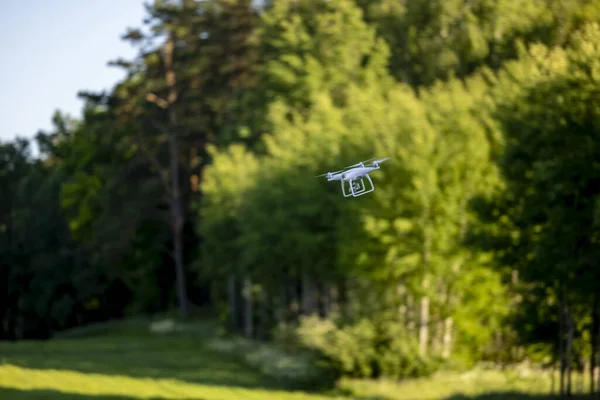 Unmanned aerial vehicle against the backdrop of green trees - a drone in the air