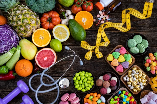 Healthy eating vs unhealthy eating with medicine pills, stethoscope and meter tape on the table. Healty lifestyle concept.