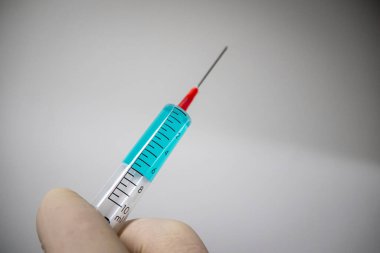 Eldivenli bir el mavi sıvıyla tıbbi bir şırınga tutuyor. 