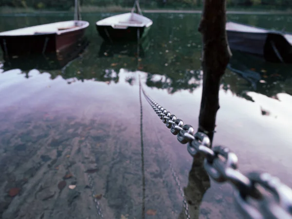 a rowing boat is attached to a steel chain, which floats on a lake